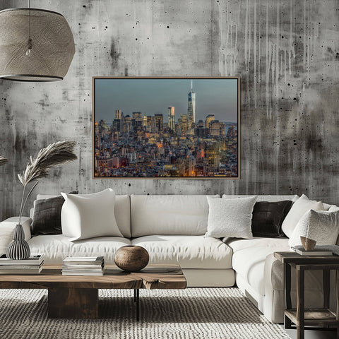 A dusk photograph of the Downtown Manhattan skyline with city lights shining on a clear blue sky.