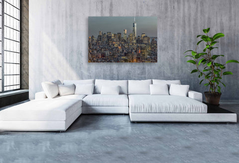 A dusk photograph of the Downtown Manhattan skyline with city lights shining on a clear blue sky.